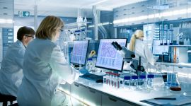 Zwei Wissenschaftler in weißen Laborkitteln arbeiten im Labor an Computern und Mikroskopen.