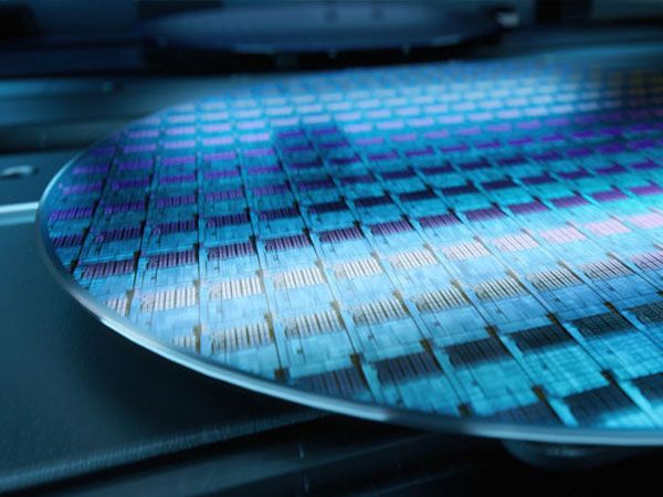 Nahaufnahme einer Silizium-Waferplatte mit vielen rechteckigen Mikrochip-Strukturen in blauen und violetten Farbtönen, Teil der Halbleiterfertigung.