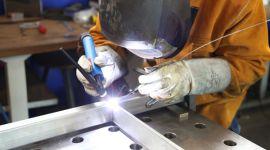 Schweißer mit Schutzmaske arbeitet an einem Metallrahmen.