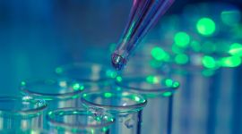 Pipette mit Flüssigkeit über Reagenzgläsern im Labor unter blau-grünem Licht
