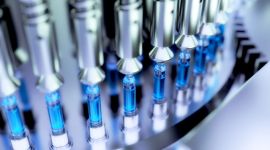 Close-up of an automated machine filling syringes with blue liquid.